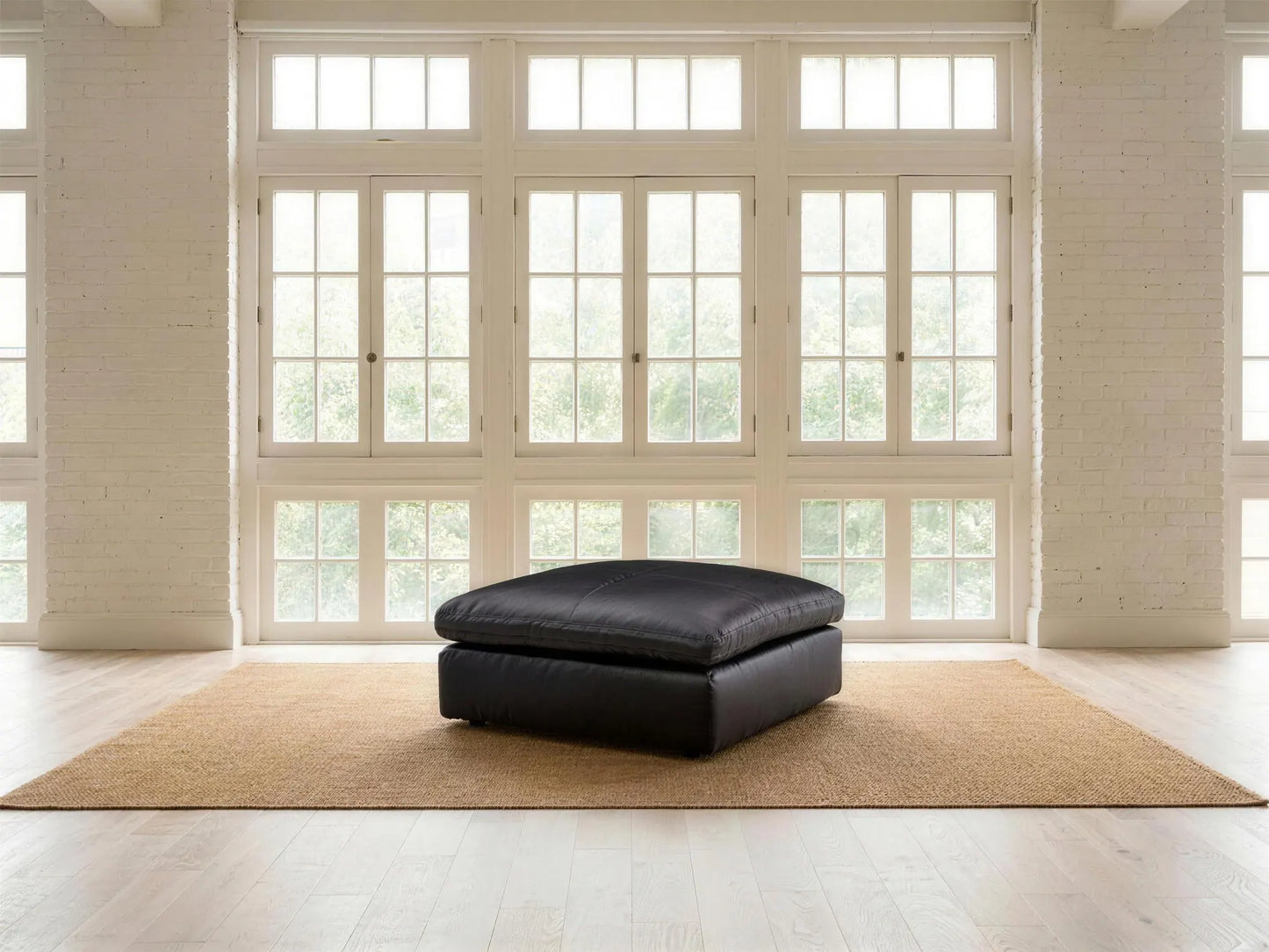 Emilia Leather Ottoman in black top-grain leather, styled in a living room